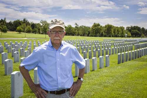 A veteran stands in front of a veteran cemetery